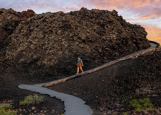 A hiker among the black lava fields of Craters of the Moon at sunset.